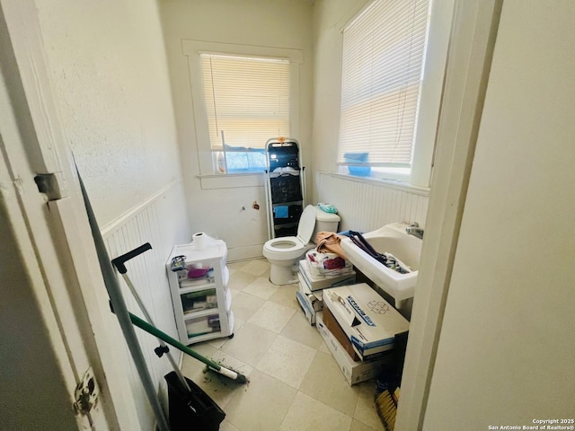 bathroom with wainscoting, toilet, and a healthy amount of sunlight