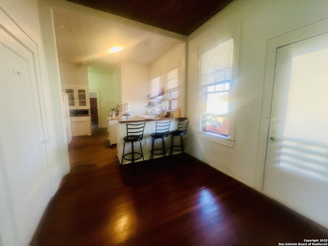 kitchen featuring a kitchen breakfast bar, a peninsula, white cabinets, and dark wood-style flooring