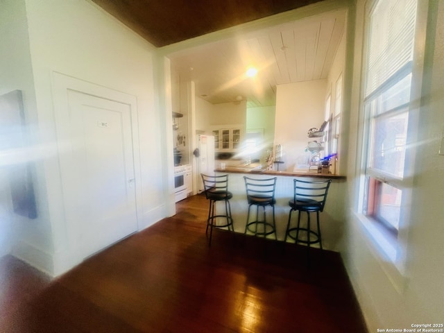 kitchen featuring dark wood-type flooring, a kitchen breakfast bar, a peninsula, and wall oven