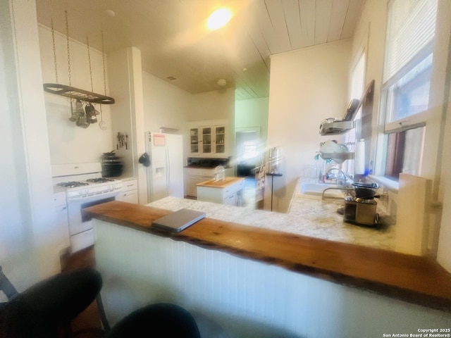 kitchen featuring white range with gas cooktop, a peninsula, a sink, white cabinets, and glass insert cabinets