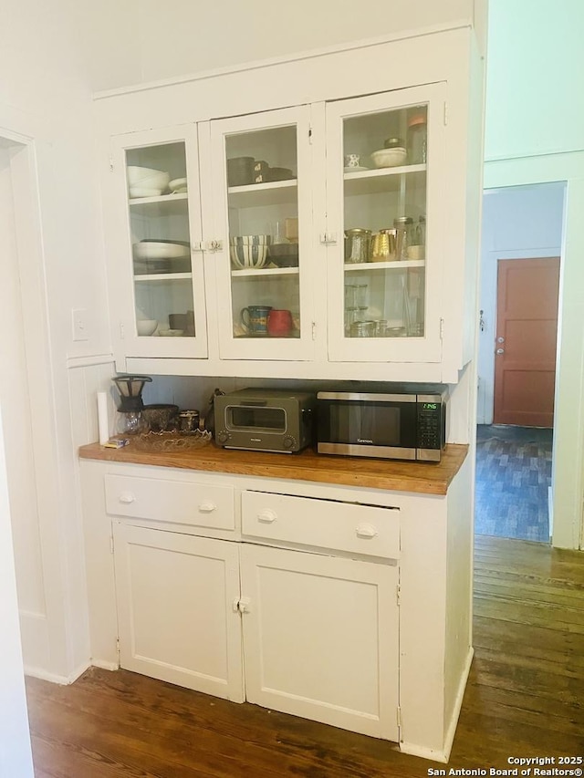 bar featuring a toaster, stainless steel microwave, and dark wood-type flooring