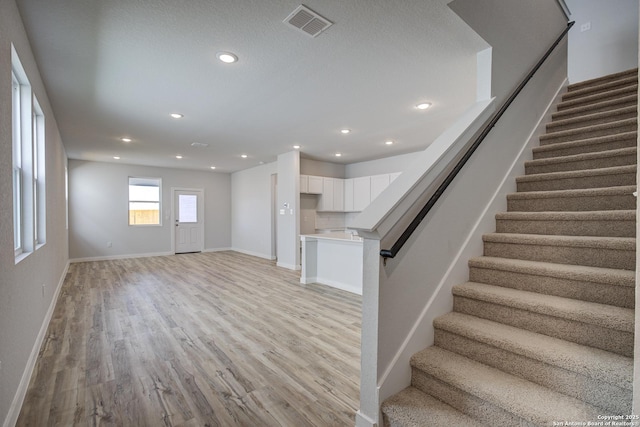 unfurnished living room with stairway, light wood-style floors, visible vents, and baseboards