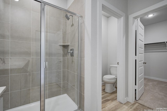 bathroom with toilet, a stall shower, wood finished floors, baseboards, and a spacious closet