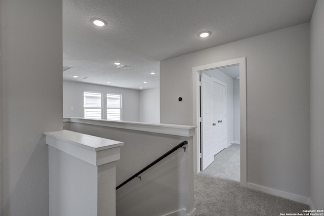 hall with carpet flooring, an upstairs landing, baseboards, and a textured ceiling