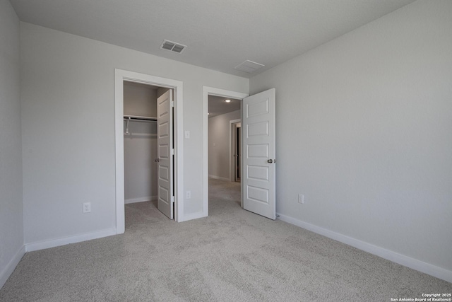 unfurnished bedroom with visible vents, a walk in closet, a closet, carpet, and baseboards