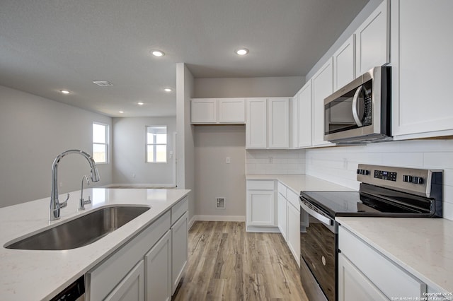 kitchen featuring light stone countertops, appliances with stainless steel finishes, white cabinetry, and a sink