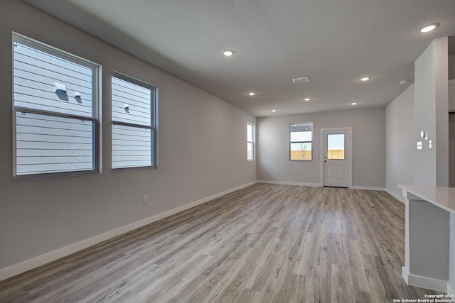 spare room with a textured ceiling, recessed lighting, baseboards, and light wood-type flooring