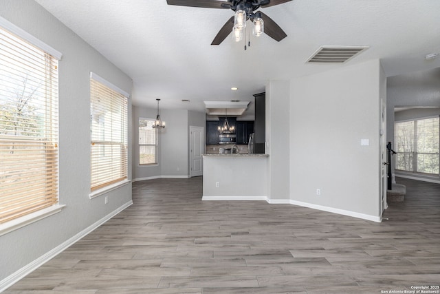 unfurnished living room with wood finished floors, ceiling fan with notable chandelier, visible vents, and a wealth of natural light
