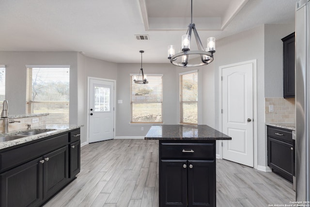 kitchen with visible vents, a sink, a tray ceiling, an inviting chandelier, and decorative backsplash