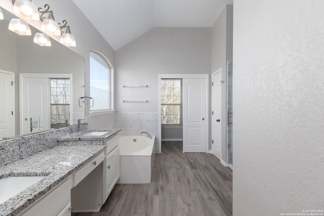 full bath with wood finished floors, double vanity, a sink, vaulted ceiling, and a bath