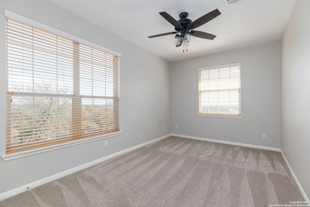 carpeted spare room with visible vents, baseboards, and ceiling fan