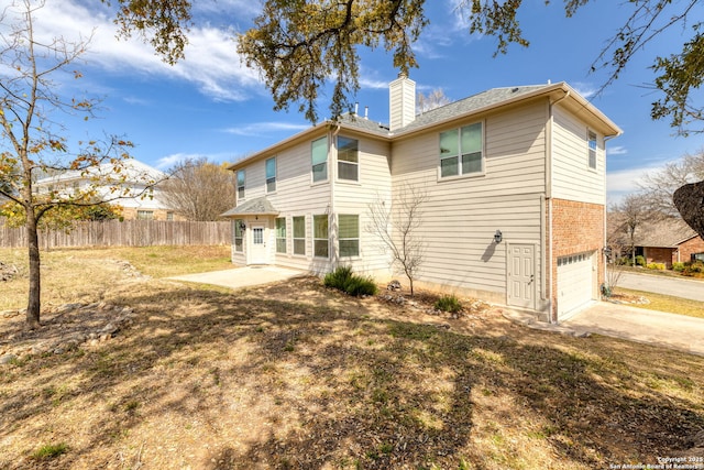 rear view of house featuring driveway, fence, an attached garage, brick siding, and a chimney