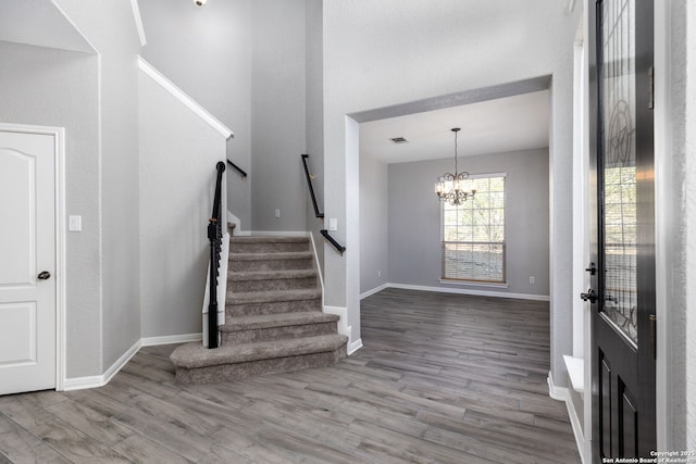 entryway with visible vents, baseboards, stairway, an inviting chandelier, and wood finished floors