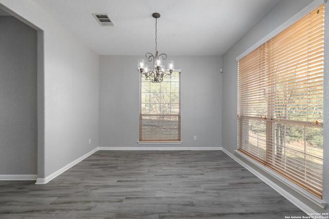 unfurnished dining area with an inviting chandelier, wood finished floors, visible vents, and baseboards