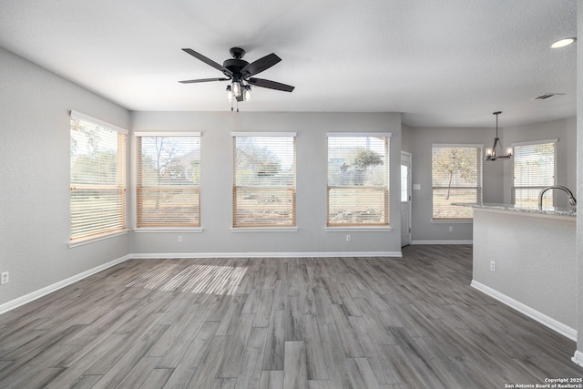 unfurnished living room featuring dark wood finished floors, ceiling fan with notable chandelier, visible vents, and baseboards