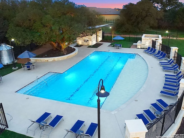 pool at dusk with a patio area, a community pool, and fence