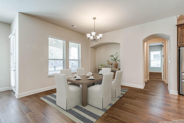 dining area with visible vents, baseboards, wood finished floors, arched walkways, and a notable chandelier