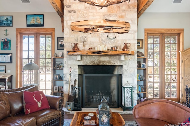 living room featuring beamed ceiling, a fireplace, visible vents, and a wealth of natural light