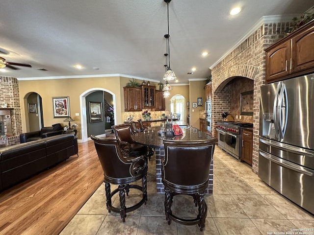 kitchen with a kitchen bar, an island with sink, a sink, arched walkways, and appliances with stainless steel finishes