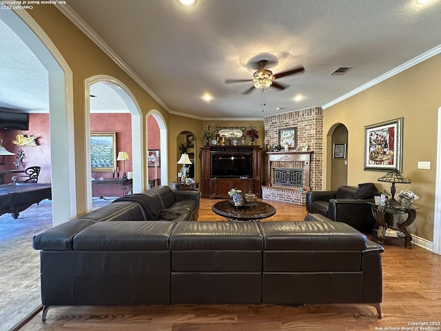 living room featuring a brick fireplace, ornamental molding, arched walkways, and ceiling fan