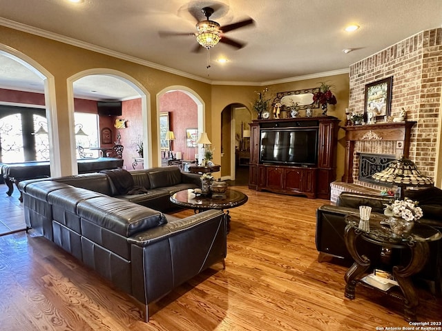 living area featuring wood finished floors, arched walkways, ornamental molding, ceiling fan, and a textured ceiling