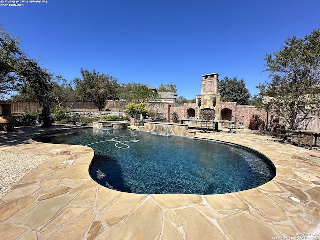 view of swimming pool with a patio, an outdoor stone fireplace, a fenced backyard, and a pool with connected hot tub