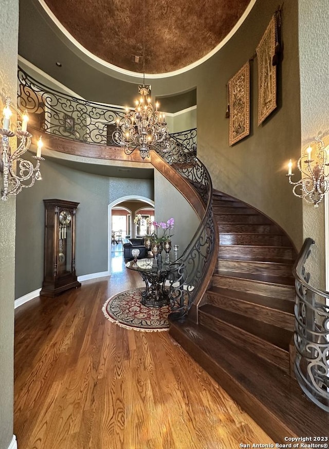 stairway featuring wood finished floors, arched walkways, a towering ceiling, a raised ceiling, and a chandelier