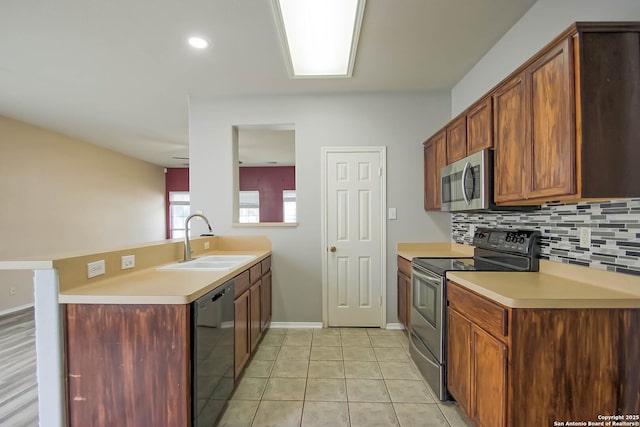 kitchen with a peninsula, a sink, decorative backsplash, light countertops, and appliances with stainless steel finishes