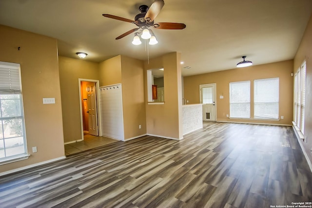 unfurnished living room with wood finished floors, plenty of natural light, a ceiling fan, and baseboards