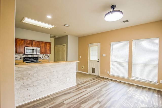 kitchen with stove, stainless steel microwave, tasteful backsplash, and visible vents