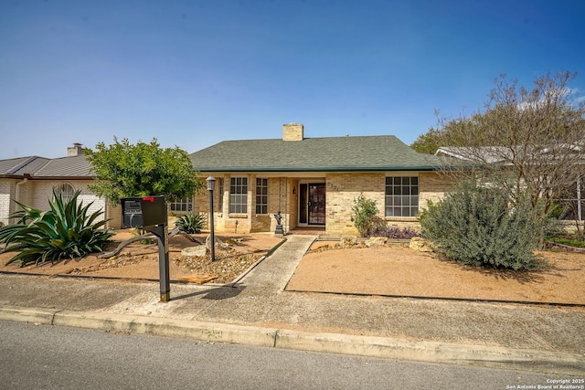 ranch-style home with a shingled roof, brick siding, and a chimney