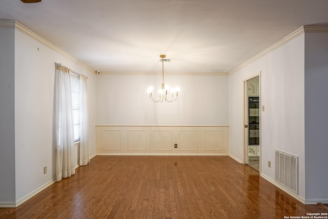 empty room featuring wood finished floors, visible vents, crown molding, a decorative wall, and a notable chandelier