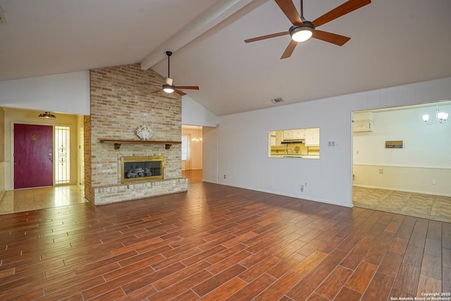 unfurnished living room with visible vents, a brick fireplace, beam ceiling, wood finished floors, and a ceiling fan