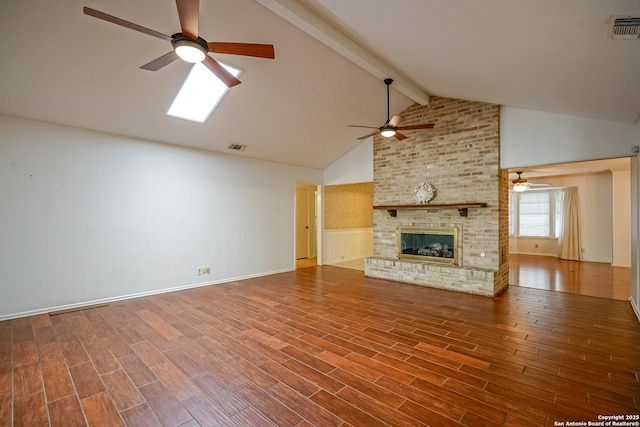 unfurnished living room featuring wood finished floors, a ceiling fan, visible vents, lofted ceiling with beams, and a brick fireplace