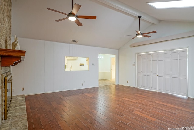 unfurnished living room with a stone fireplace, lofted ceiling with beams, wood finished floors, and ceiling fan