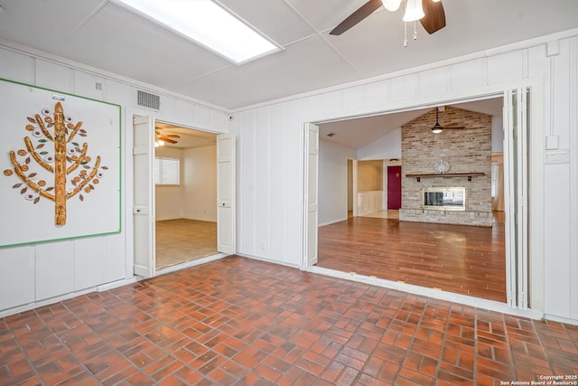 unfurnished living room with visible vents, a brick fireplace, ceiling fan, lofted ceiling, and brick floor