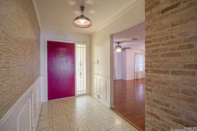 foyer entrance with brick wall, a wainscoted wall, ornamental molding, light tile patterned floors, and a decorative wall