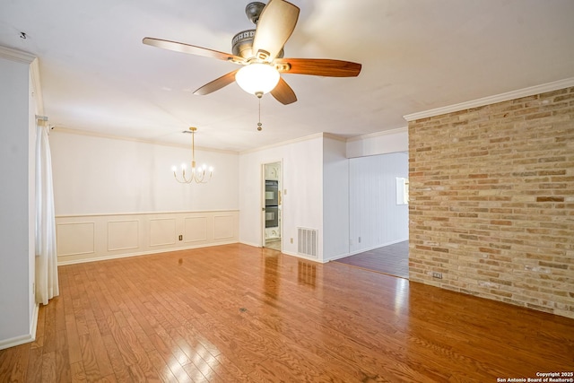 unfurnished room featuring visible vents, brick wall, ornamental molding, ceiling fan with notable chandelier, and wood finished floors