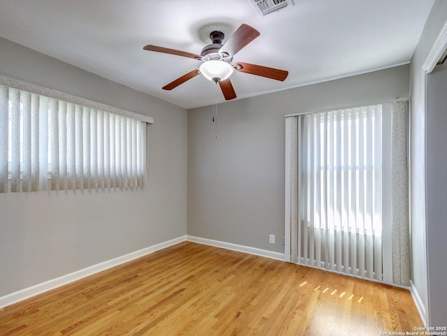 empty room with ceiling fan, wood finished floors, visible vents, and baseboards