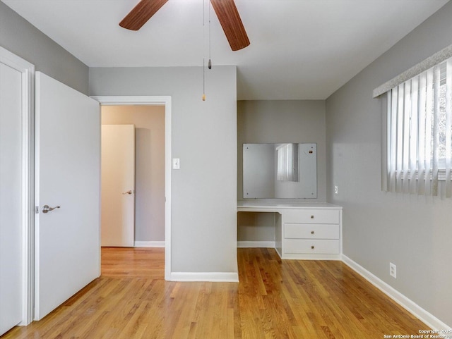 unfurnished bedroom with baseboards, ceiling fan, built in study area, and light wood-style floors