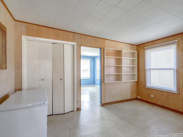 interior space with baseboards, built in shelves, wooden walls, and crown molding