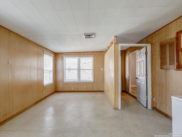 empty room featuring visible vents, light floors, baseboards, and wood walls