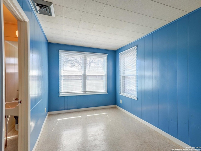 spare room with visible vents, wood walls, and baseboards