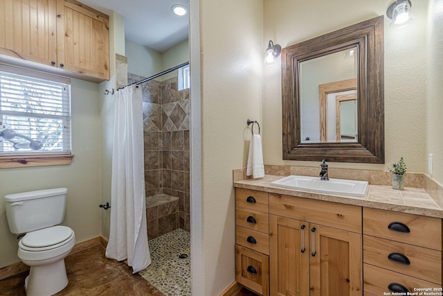 full bath featuring a tile shower, toilet, vanity, and baseboards