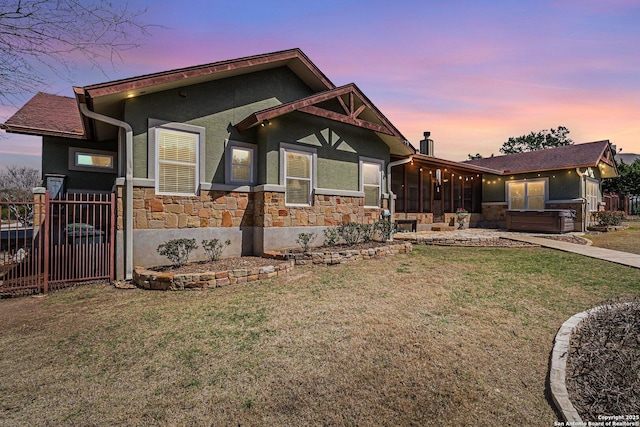 view of front of home featuring stone siding, stucco siding, a front yard, and a sunroom