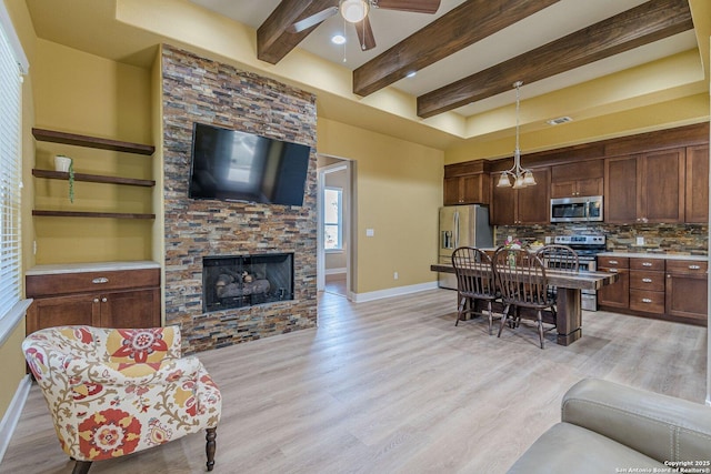 living room with beam ceiling, a ceiling fan, a stone fireplace, light wood finished floors, and baseboards