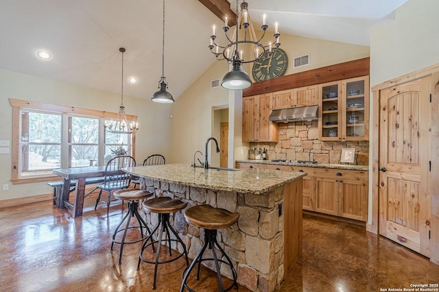 kitchen with under cabinet range hood, a sink, concrete floors, an inviting chandelier, and decorative backsplash