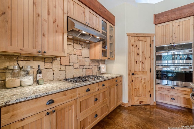 kitchen with tasteful backsplash, light stone countertops, under cabinet range hood, light brown cabinetry, and appliances with stainless steel finishes