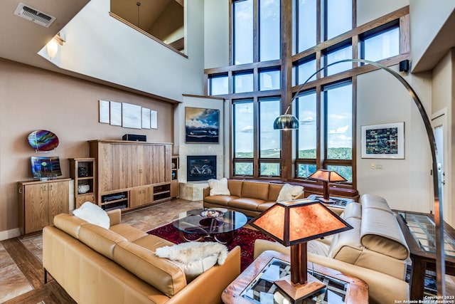 living room with a tiled fireplace, baseboards, visible vents, and a towering ceiling