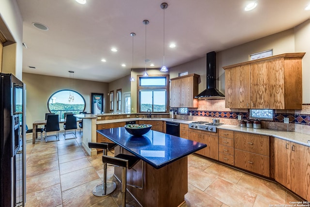 kitchen featuring pendant lighting, black appliances, a peninsula, wall chimney exhaust hood, and decorative backsplash